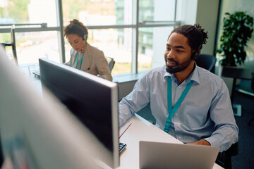 Happy black entrepreneur multitasking while working on desktop PC and laptop in  office.