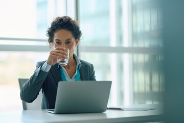 Businesswoman having  glass of water while working on laptop in office.