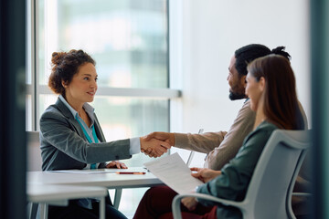 Bank manager shaking hands with her clients during  meeting in office.