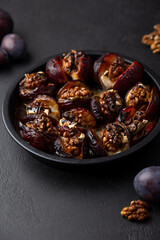 Plums baked with Camembert cheese, walnuts and honey on a black plate. Popular hot appetizer. Selective focus, close-up.
