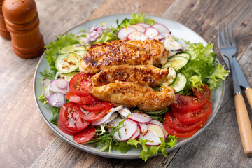 Warm salad with baked chicken breast and fresh vegetables, dressed with olive oil on a wooden background. Home kitchen in rustic style. Hearty delicious food. Selective focus, close-up.
