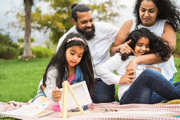 Happy indian family having fun painting with children outdoor at city park - Spring time and parenthood concept - Focus on female kid face