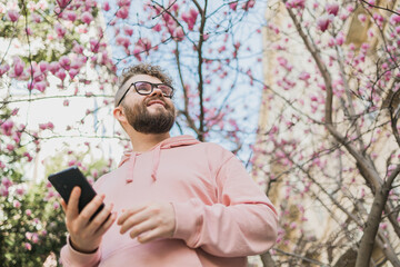 Spring day. Bearded man in pink shirt talking by phone. Spring pink sakura blossom. Handsome young...
