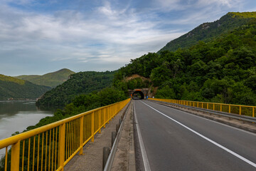 The river flows beneath, and the mountains in the background are lush with greenery, creating a peaceful and remote scene.