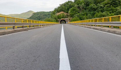  A straight asphalt road with yellow guardrails on both sides leads towards a tunnel entrance,...