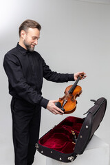 Bearded man artist packing musical instrument in violin case