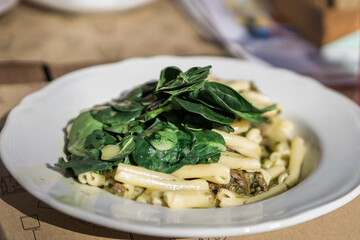 Spring pasta penne with basil pesto and sweet pea in a bowl on a rustic wooden background in street cafe