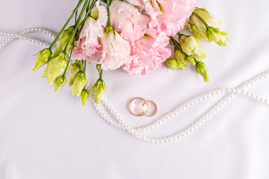 Two gold classic wedding rings on a white satin background with fresh pink austoma flowers. A copy space. postcard. invitation. cover