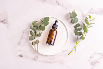 Cosmetic bottle with natural face and body care product with eucalyptus oil extract on a white round tray. Marble background. Blank product mockup.