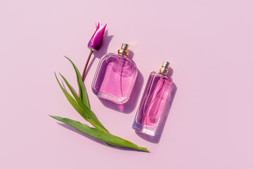 Two different bottles of perfume or eau de toilette on a lilac background with a tulip. Top view....