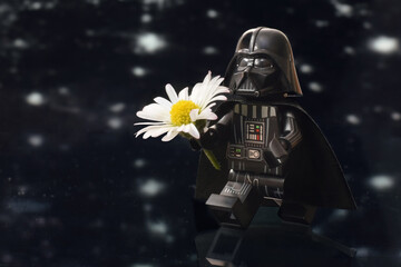 Naklejka premium Lego minifigure of Darth Vader or Star Wars male army is walking with daisy flower isolated on black. Editorial illustrative image to Mother's Day.