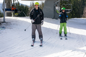 Dad and son skiers begin to descend from a mid-level ski slope. Active recreation. Healthy lifestyle