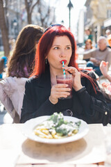 Beautiful happy woman with long red hair enjoying cocktail in a street cafe