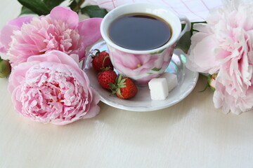 A cup of morning coffee for breakfast, pink peonies flowers on the table.