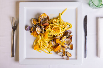 Spaghetti con sugo di vongole veraci, prezzemolo e pomodori gialli serviti in un ristorante elegante come primo piatto - obrazy, fototapety, plakaty