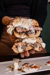 Panino da pub ripieno di hamburger di manzo, melanzane a funghetto, basilico fresco e burrata pugliese tagliato a metà e tenuto tra le mani da una cliente