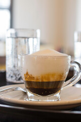 Caffè schiumato in tazza di vetro servito in un bar con accompagnato un bicchiere d'acqua frizzante
