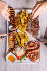 Due clienti di una braceria che si dividono una grigliata di carne mista con contorno di patate al forno, rucola, pomodori, scaglie di parmigiano e salsa agrodolce