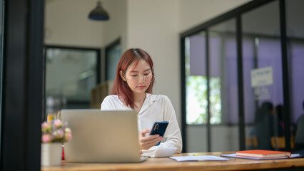A woman is sitting at a desk with a laptop and a cell phone