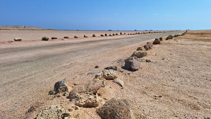 A road in a desert area fenced with homemade made of stones