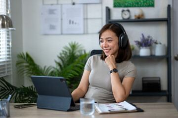 Obraz premium A woman wearing headphones is sitting at a desk with a laptop and a tablet. She is smiling and she is enjoying her work