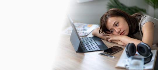 A woman is laying on a desk with a laptop and a cell phone. She is tired and is looking at the...