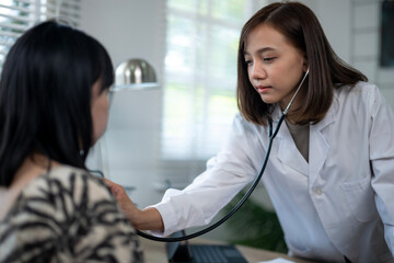 A woman doctor is examining a woman in a hospital room. The woman is wearing a white coat and the doctor is wearing a white coat. The doctor is using a stethoscope to listen to the woman's heartbeat