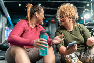 Two plus-size women embrace their bodies as they engage in a challenging workout, relaxing and talking after workout.	
