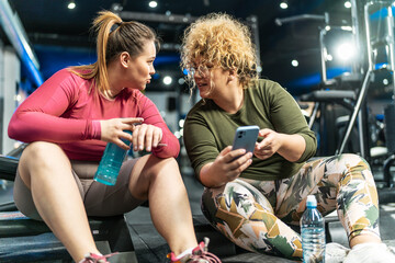 Two plus-size women embrace their bodies as they engage in a challenging workout, relaxing and talking after workout.	
