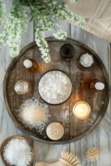 Fototapeta premium Top-view shot of a weathered wooden tray with bath products arranged in a circle: essential oils, a loofah, bath salts, and a lit candle in the center