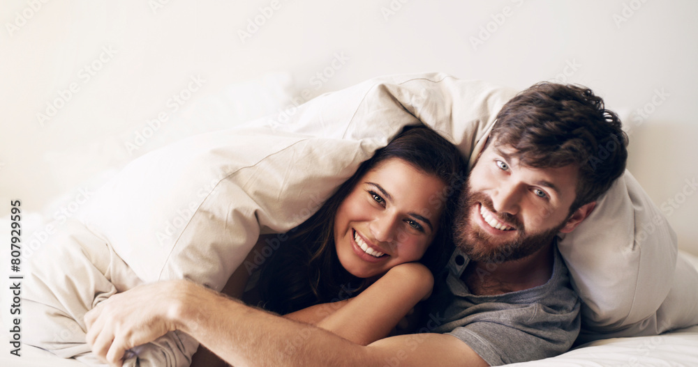 Sticker Happy, bed and couple portrait at morning with hug at home with love, marriage and cuddling together. Smile, bonding and blanket fort in a bedroom in a house with care and romance with cotton duvet