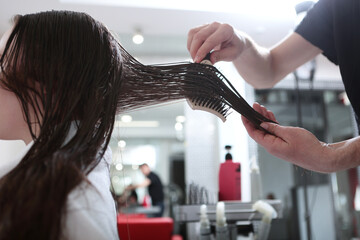 Wet hair is calculated with a comb. Hair care in a beauty salon. A woman with long, dark, matted...