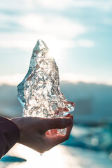 Hand holds a large piece of ice. Frozen water melts in the sun. Light reflections, sunset, melting...