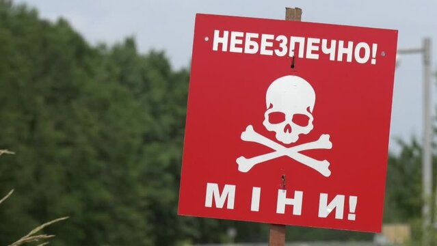 A red warning sign with an inscription is mined against the background of a green forest. The concept of humanitarian demining. Consequences of hostilities. Russian-Ukrainian war.