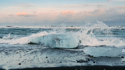 Sea waves crash on huge pieces of ice. Arctic climate, diamond beach, icebergs, melting ice, climate change, sunset.