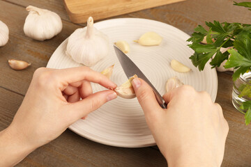 Woman peeling fresh garlic at table, closeup