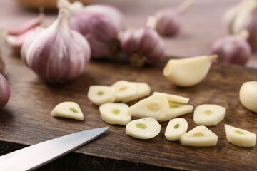 Pieces of fresh garlic and knife on table, selective focus