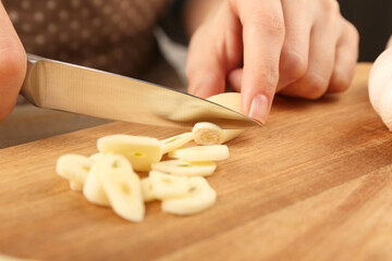 Woman cutting fresh garlic at table, selective focus
