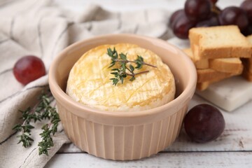 Tasty baked camembert in bowl, thyme, grapes and croutons on wooden table, closeup