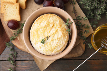 Tasty baked camembert in bowl, thyme honey, croutons and grapes on wooden table, flat lay