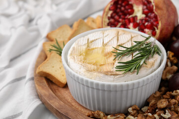 Board with tasty baked camembert and rosemary in bowl on table, closeup. Space for text