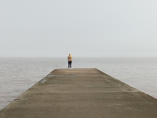 Man alone fishing on a pier, seen in the distance on a cloudy day