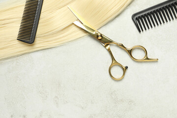Professional hairdresser scissors and comb with blonde hair strand on grey table, top view. Space...