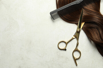 Professional hairdresser scissors and comb with brown hair strand on grey table, top view. Space...