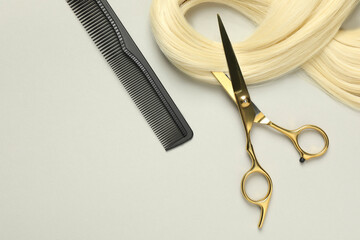 Professional hairdresser scissors and comb with blonde hair strand on light grey background, flat...