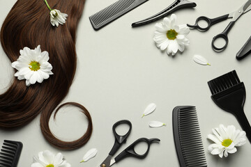 Flat lay composition with professional hairdresser tools, flowers and brown hair strand on light...