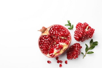 Cut fresh pomegranate and green leaves on white background, flat lay. Space for text