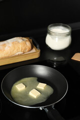 Melting butter in frying pan, bread and flour on black table