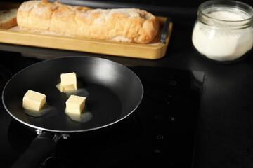 Melting butter in frying pan, bread and flour on black table