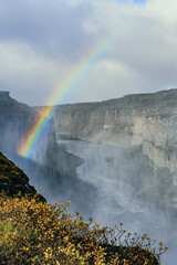 Long rainbow over a large waterfall. Sunlight, refraction with water drops, lucky moment, vivid colors.